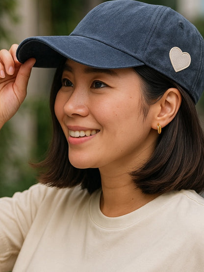 Woman wearing a blue cap with a heart emblem, smiling outdoors.